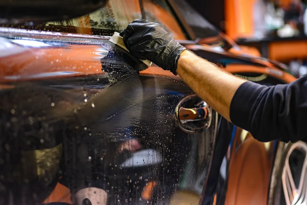 Gloved hand hand-washing the paint of an orange car